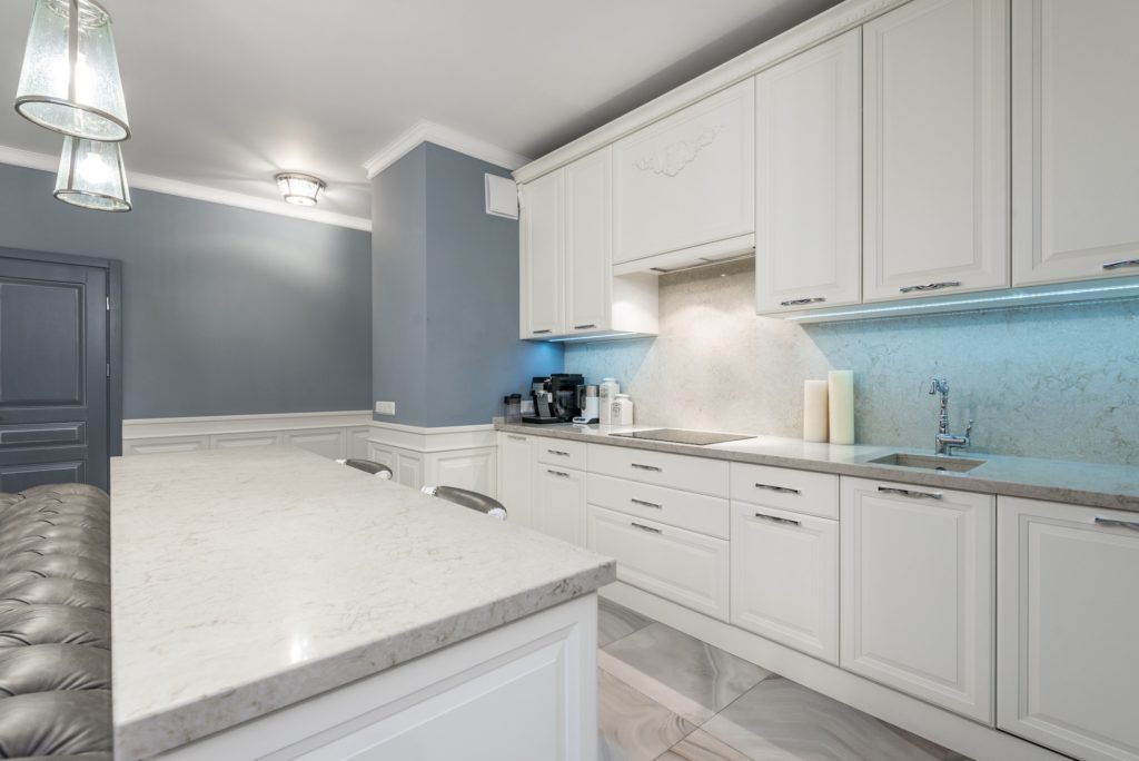 A kitchen with light-grey marble countertops and white cabinets.