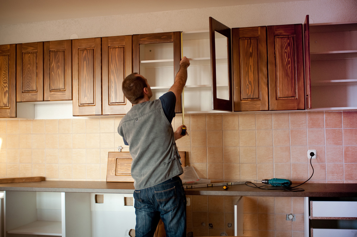A person measuring brown wooden cabinets in a kitchen in El Paso.